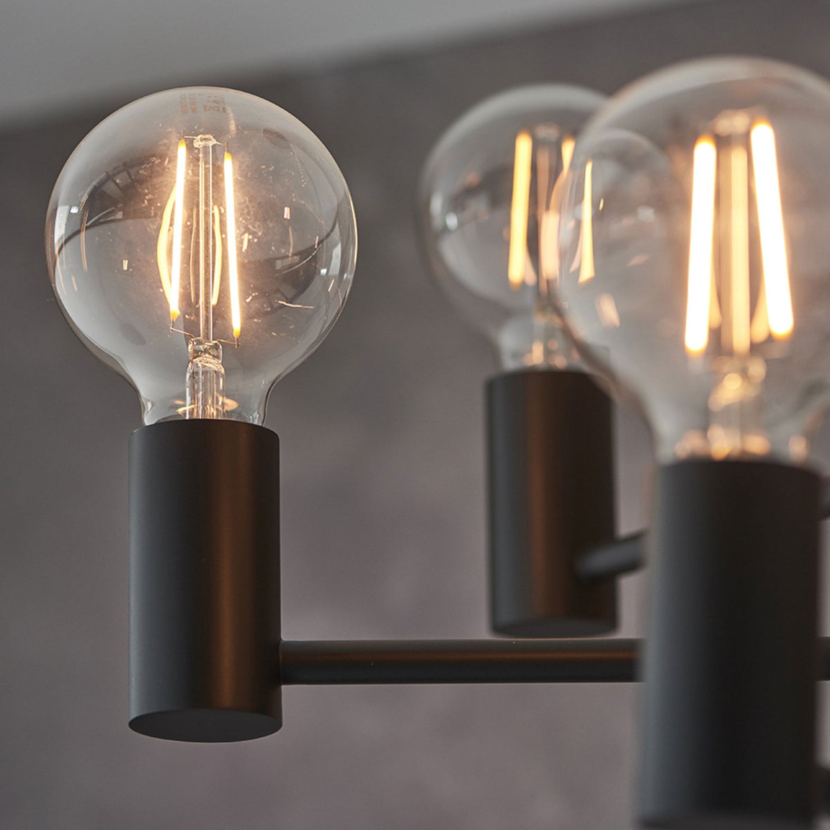 Close-up of an exposed bulb on a black chandelier, with other bulbs blurred in the background.