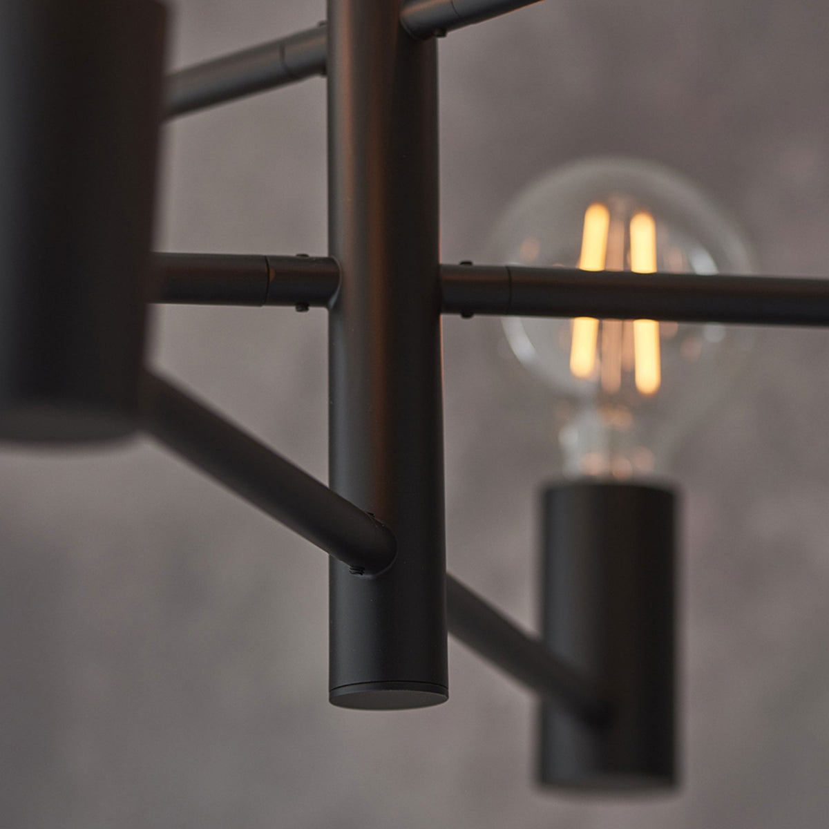 Close-up of the black metal frame of a chandelier with a blurred exposed bulb in the background.