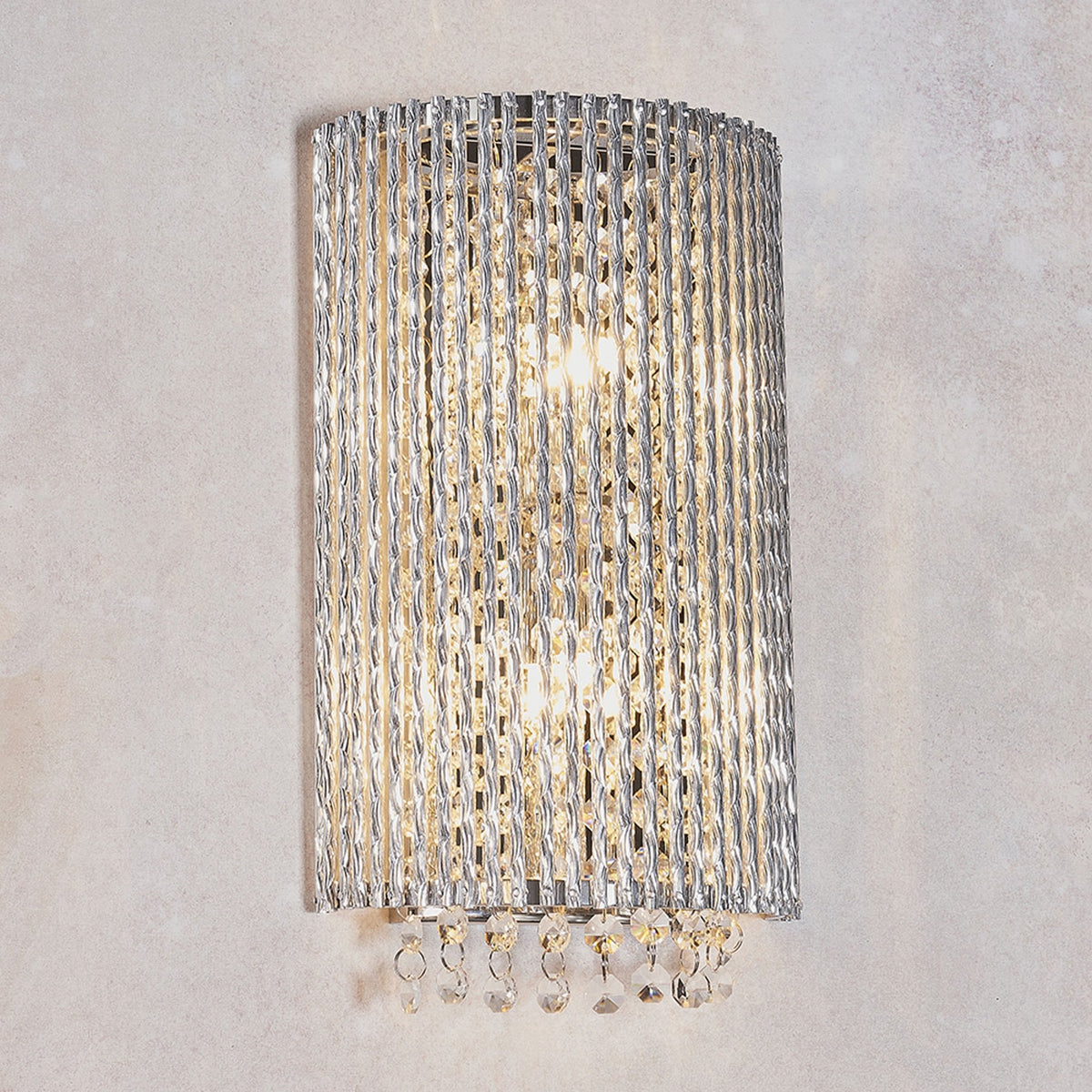 A curved wall light with vertical clear glass rods and crystal drops, illuminated on a light wall.