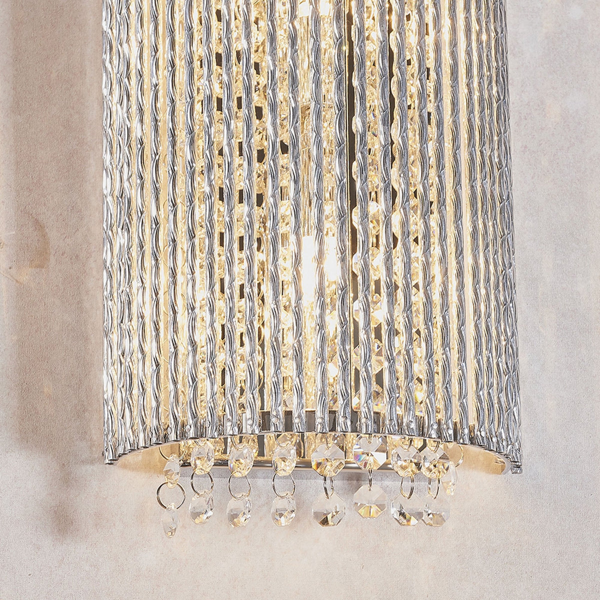 Close-up of the bottom of a curved wall light with vertical clear glass rods and hanging crystal drops.