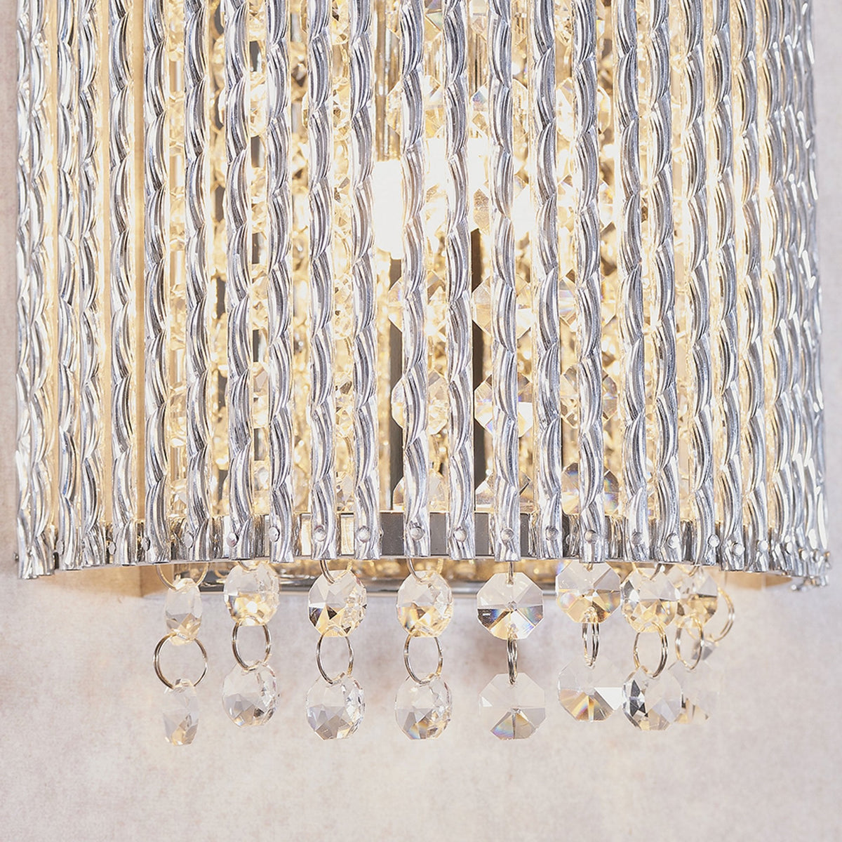 Close-up of the bottom of a curved wall light with vertical clear glass rods and hanging crystal drops.