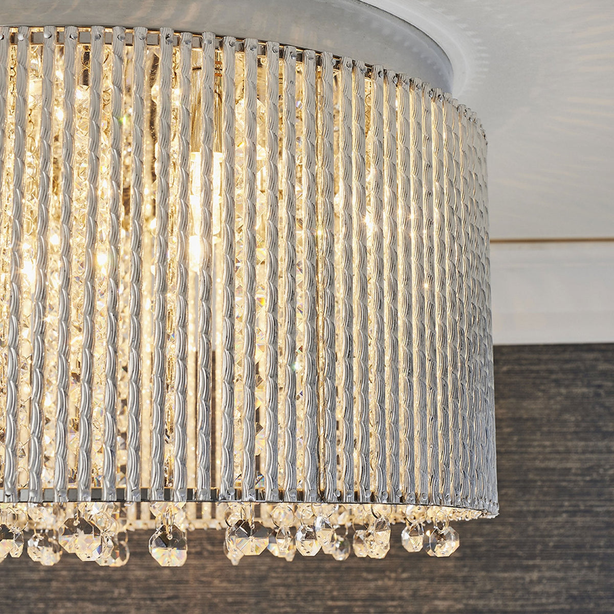 Side view of a round, silver flush mount ceiling light with a textured band and dangling crystal accents.