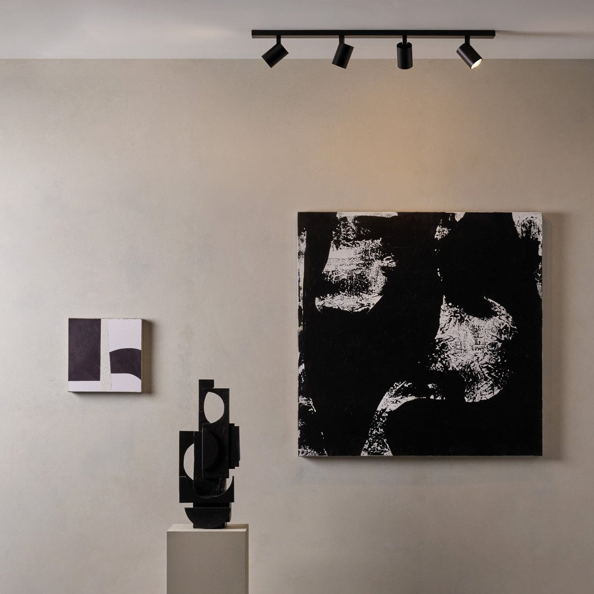 Black track lighting with four spotlights illuminating abstract black and white artwork and sculpture