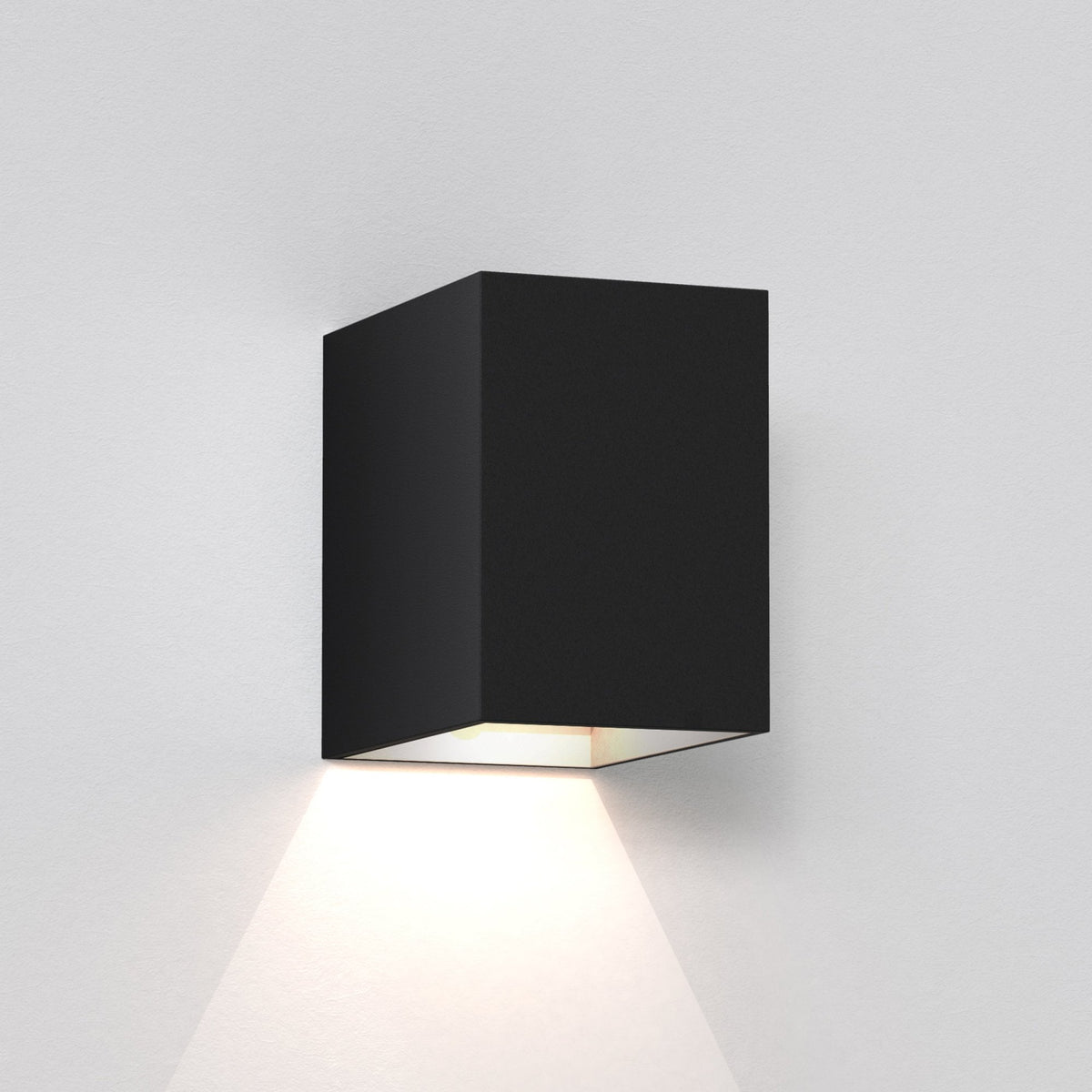Black rectangular wall light fixture casting a warm glow downwards on a white textured wall