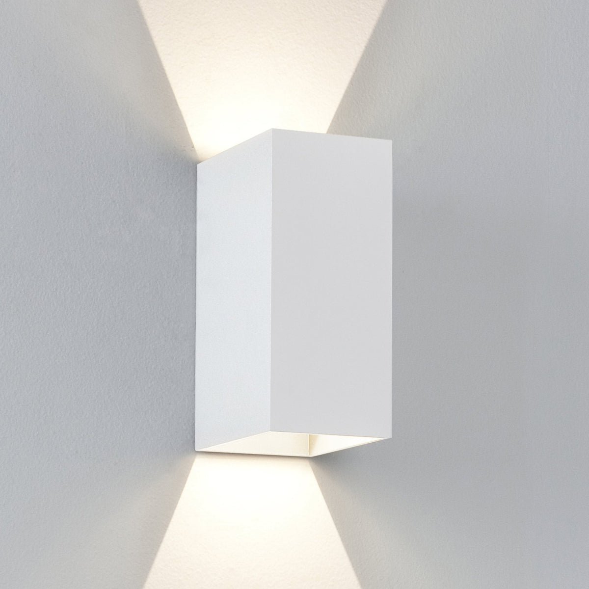 White rectangular wall light fixture casting light upwards and downwards on a grey wall