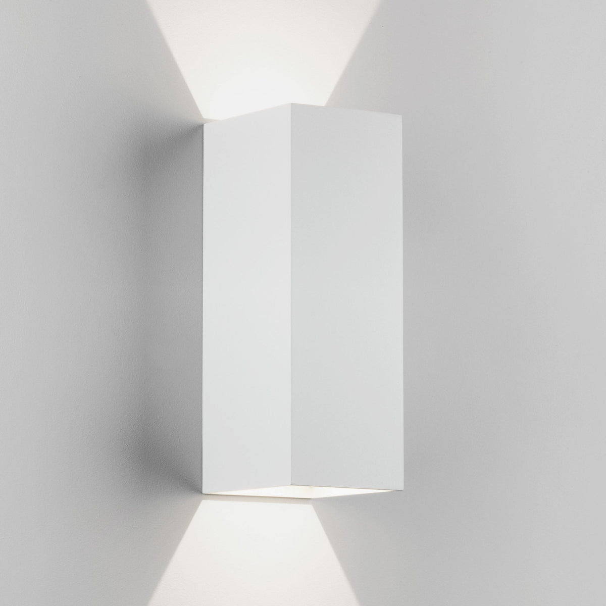 White rectangular wall light fixture casting light upwards and downwards on a white wall
