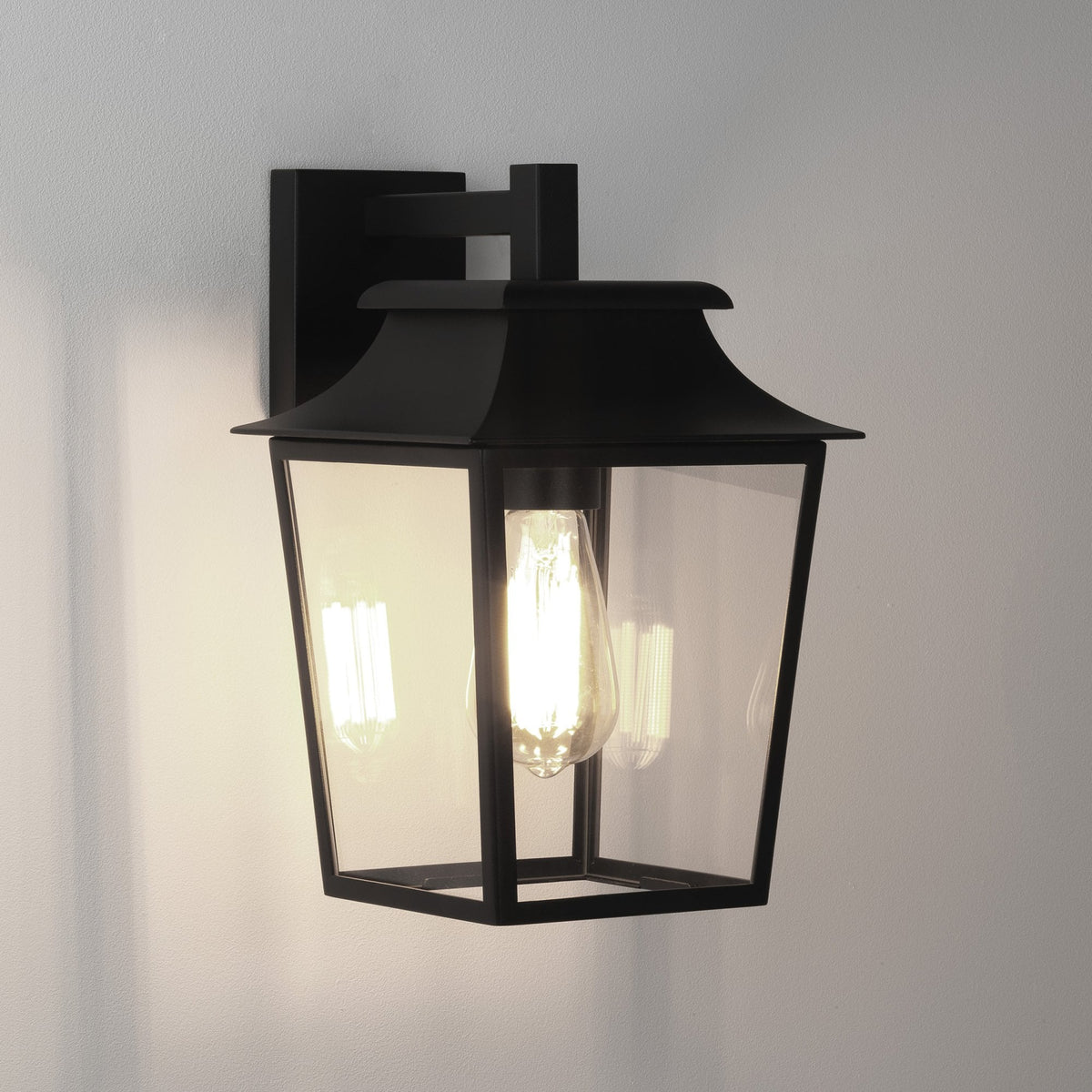 Black outdoor wall light with clear glass panels and an exposed filament bulb