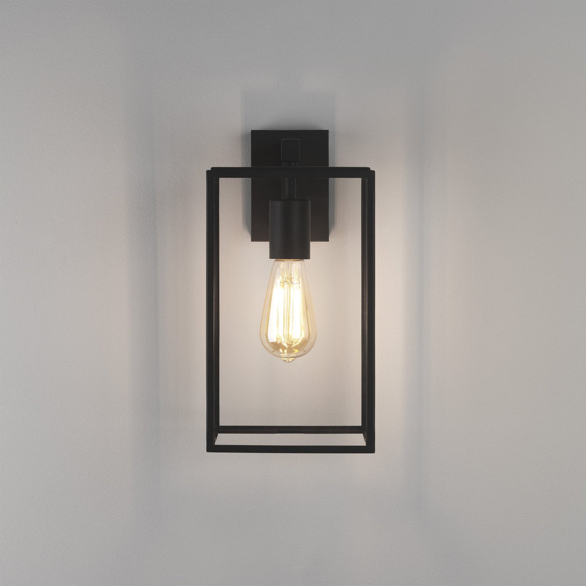 Black metal wall sconce with an exposed Edison bulb, casting a warm glow on a white wall
