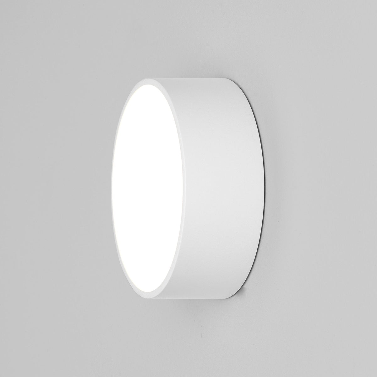Round white wall light with a glowing front, mounted on a light gray wall