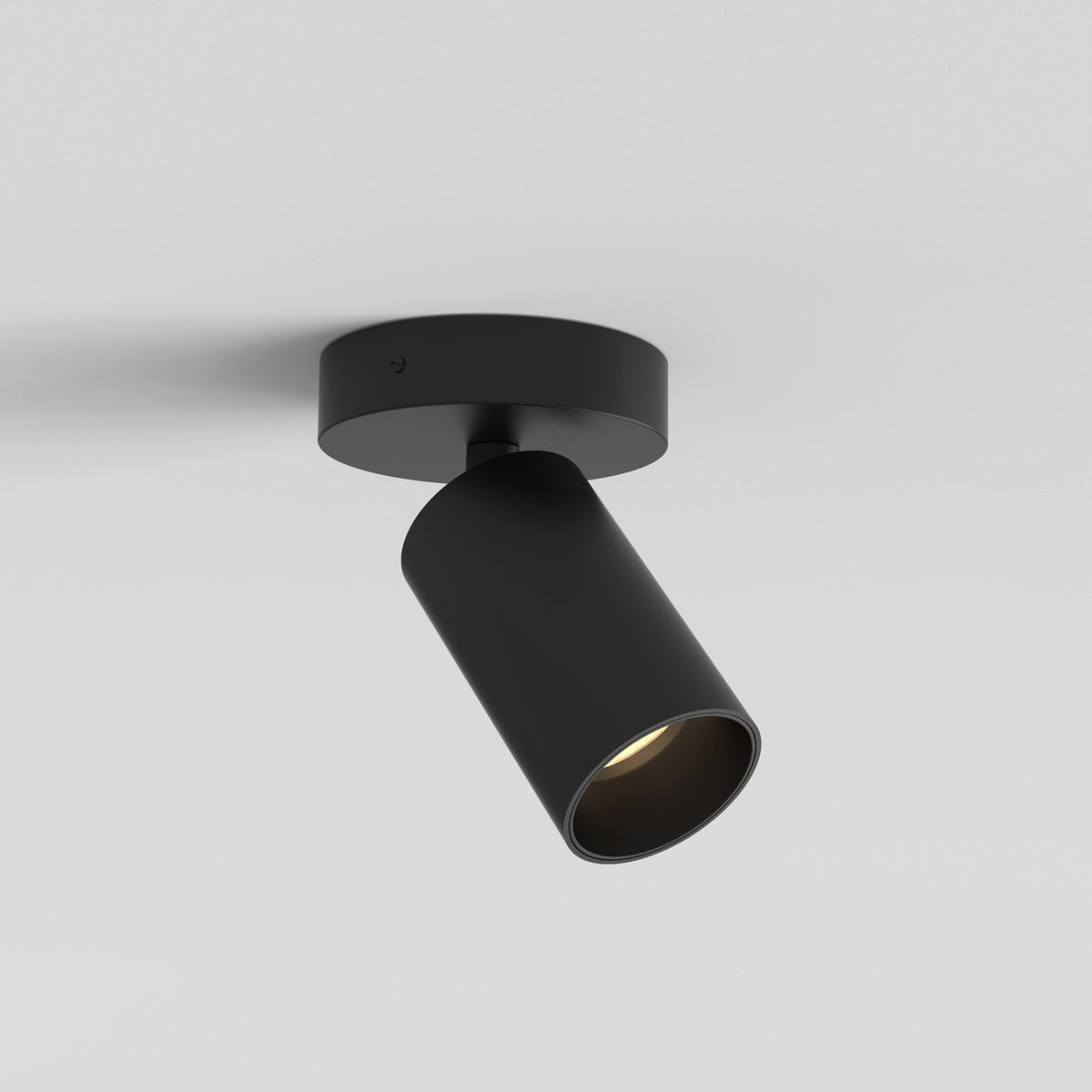 Black ceiling spotlight with a cylindrical head angled downwards, mounted on a white ceiling