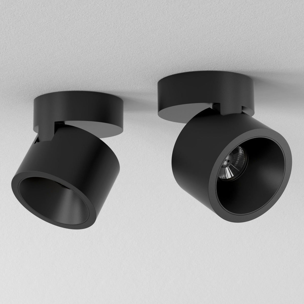 Two black cylindrical ceiling spotlights, one angled left and one angled right, on a white textured ceiling