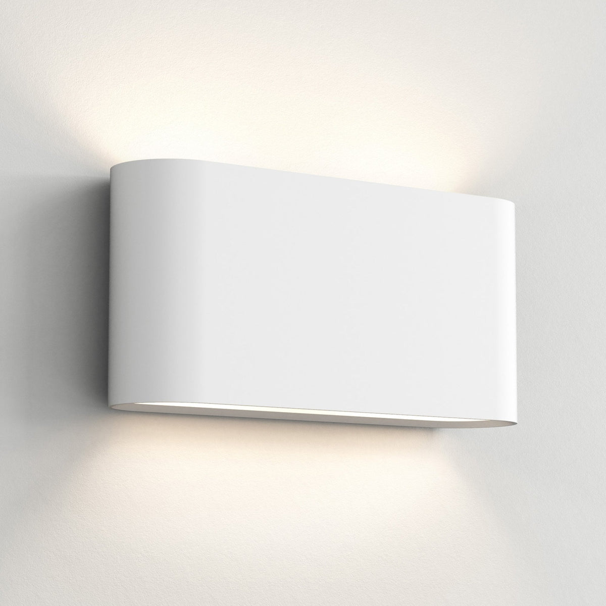 White rectangular wall light with rounded edges, casting light upwards and downwards on a textured white wall