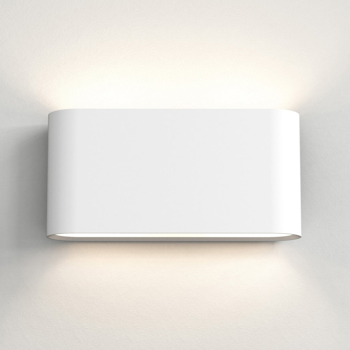 White oval wall light fixture casting light upwards and downwards on a textured white wall