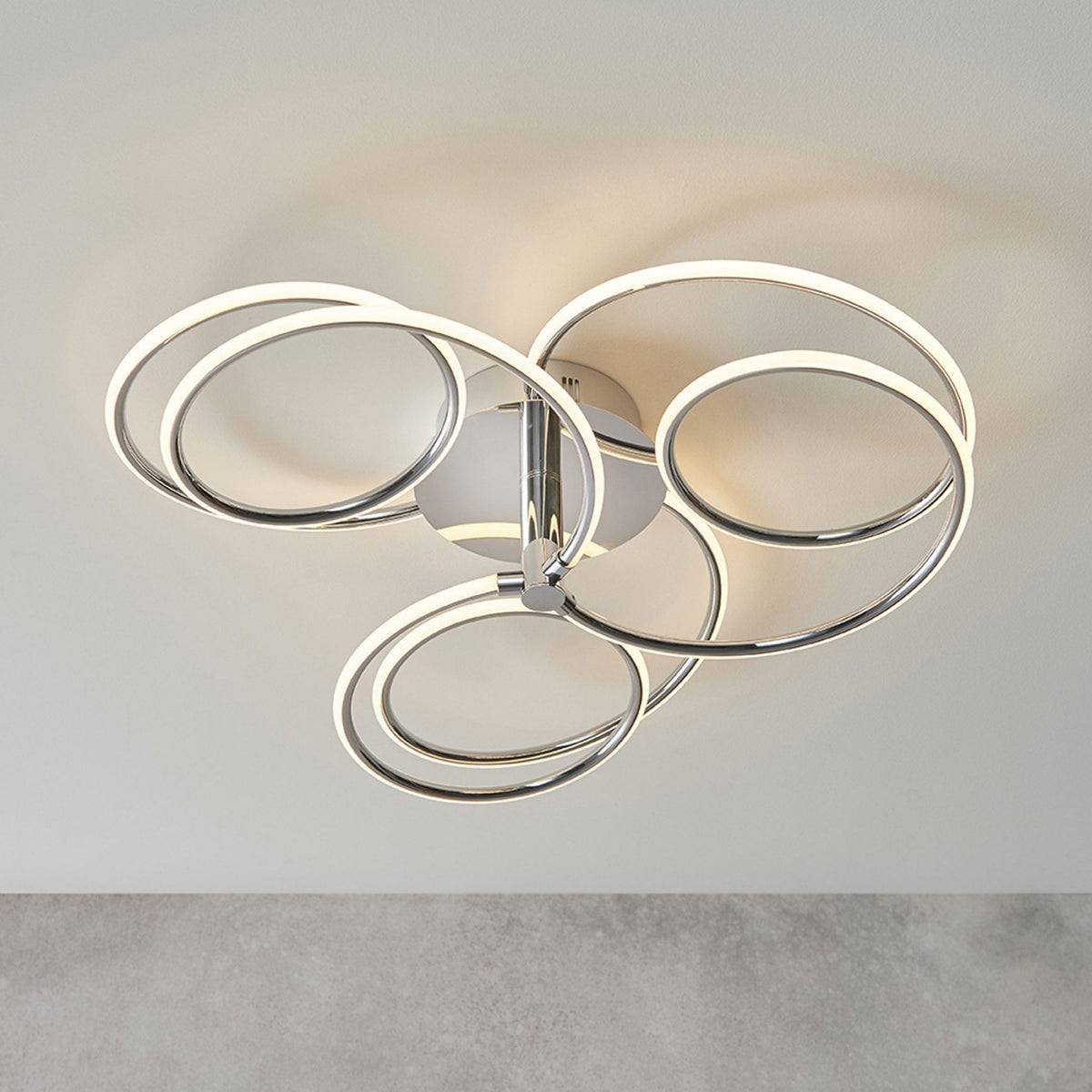 Modern chrome ceiling light with five illuminated rings in a swirling design.