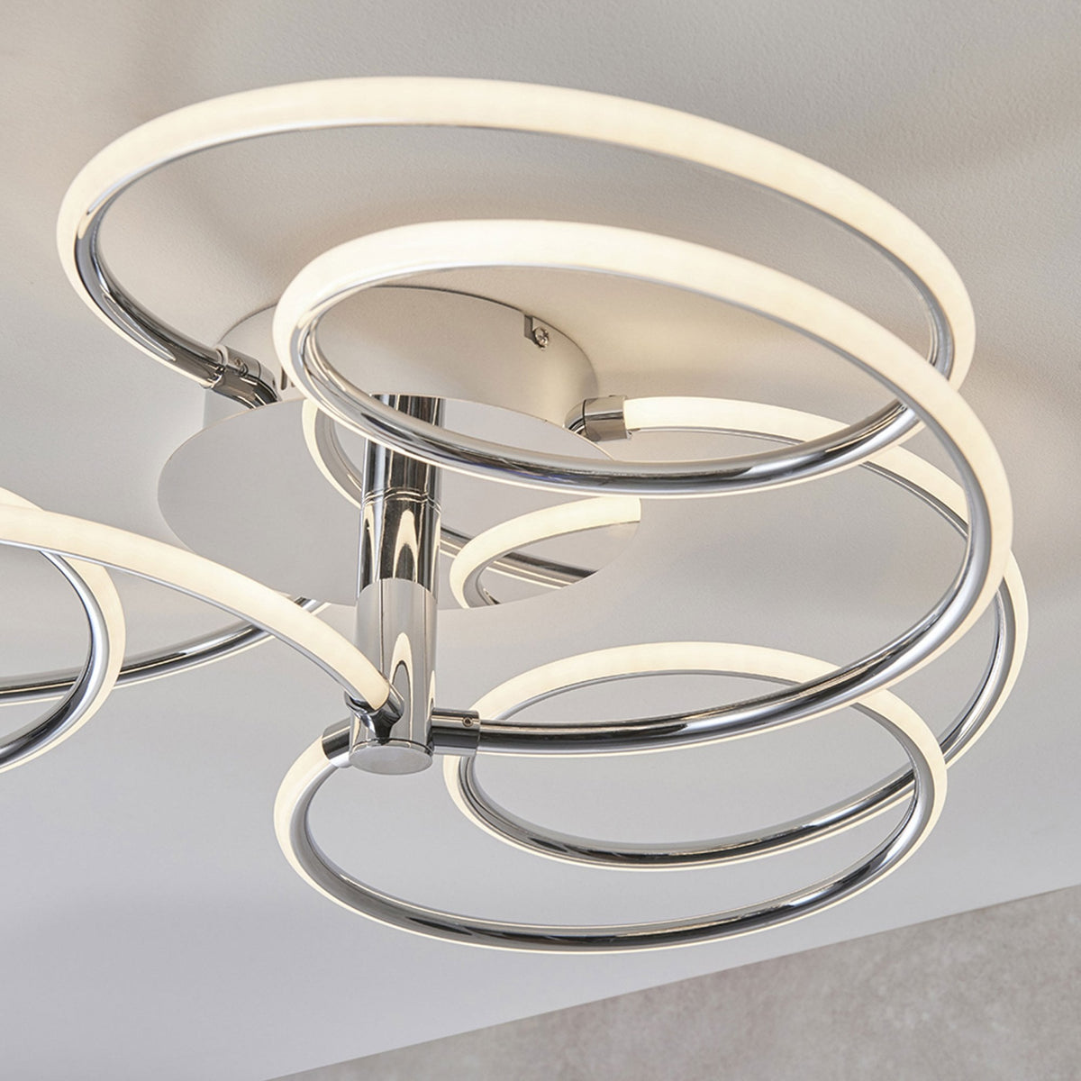 Close-up of a modern chrome ceiling light with five illuminated rings in a swirling design.