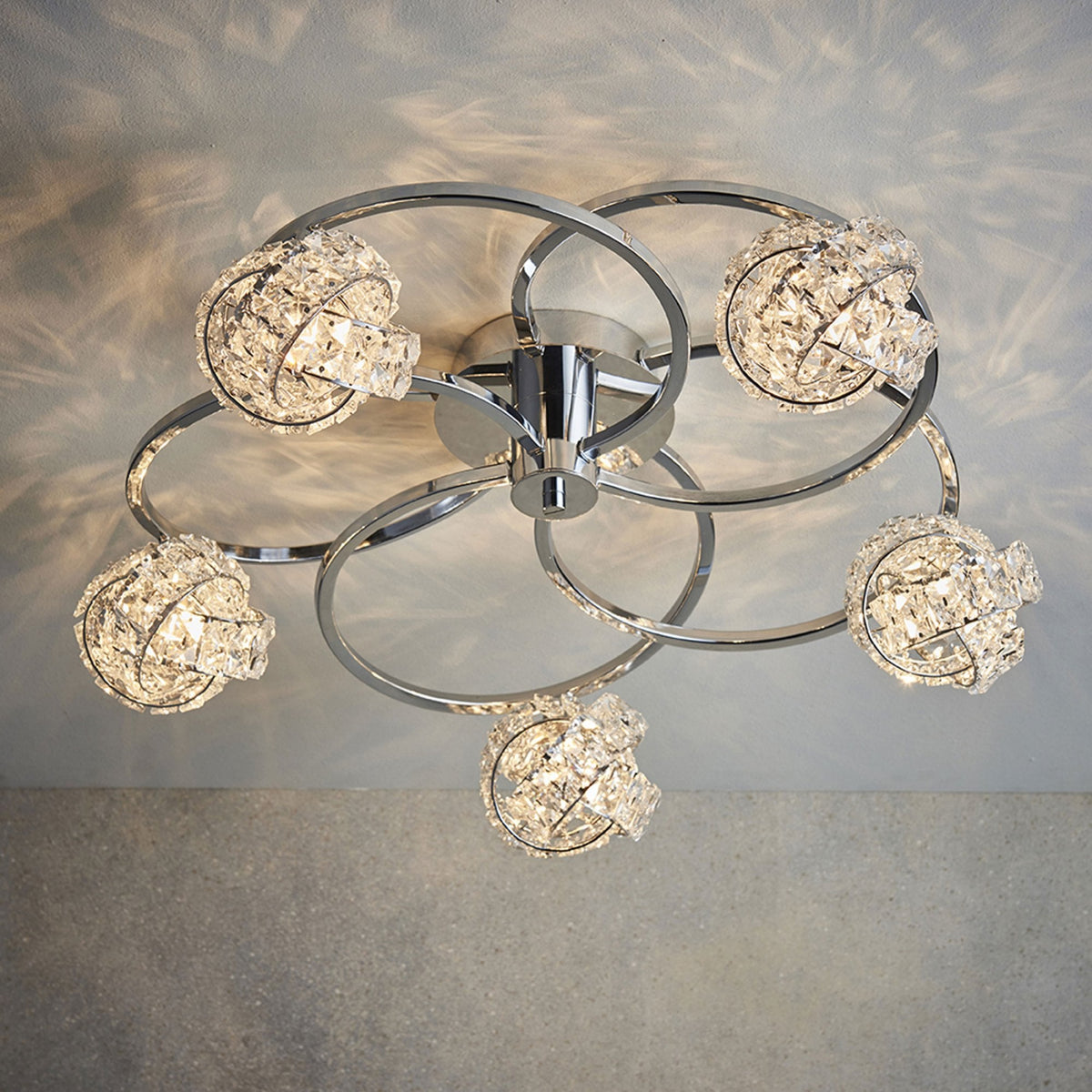 Chrome ceiling light with five crystal sphere shades, casting light patterns on the ceiling.