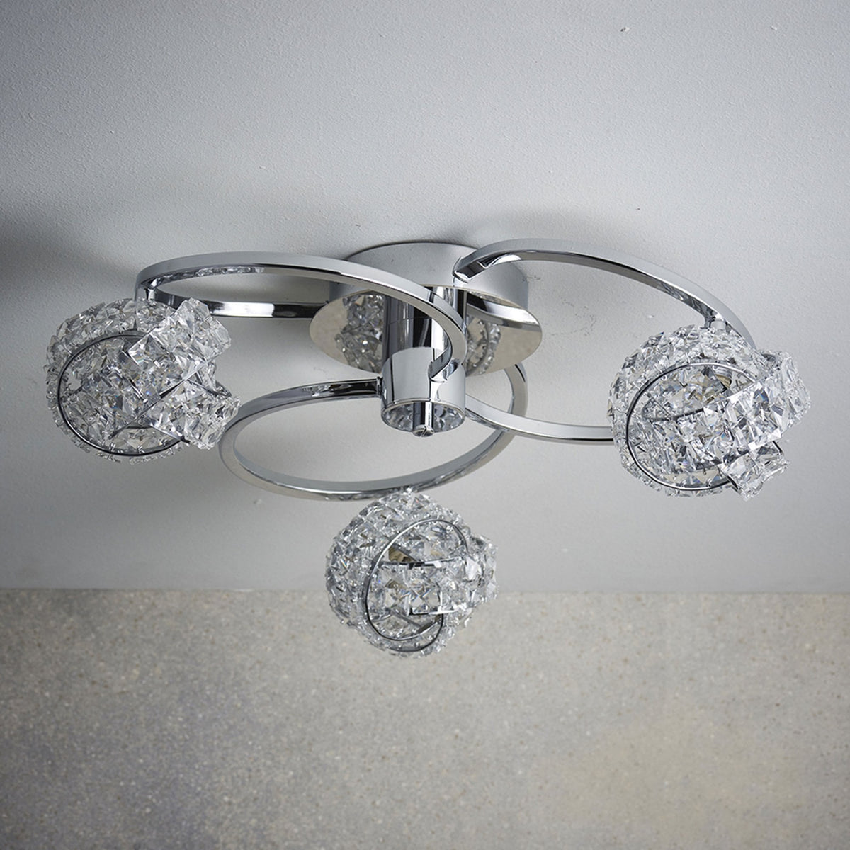 Chrome ceiling light with three crystal orb shades, unlit, mounted on a light grey ceiling.