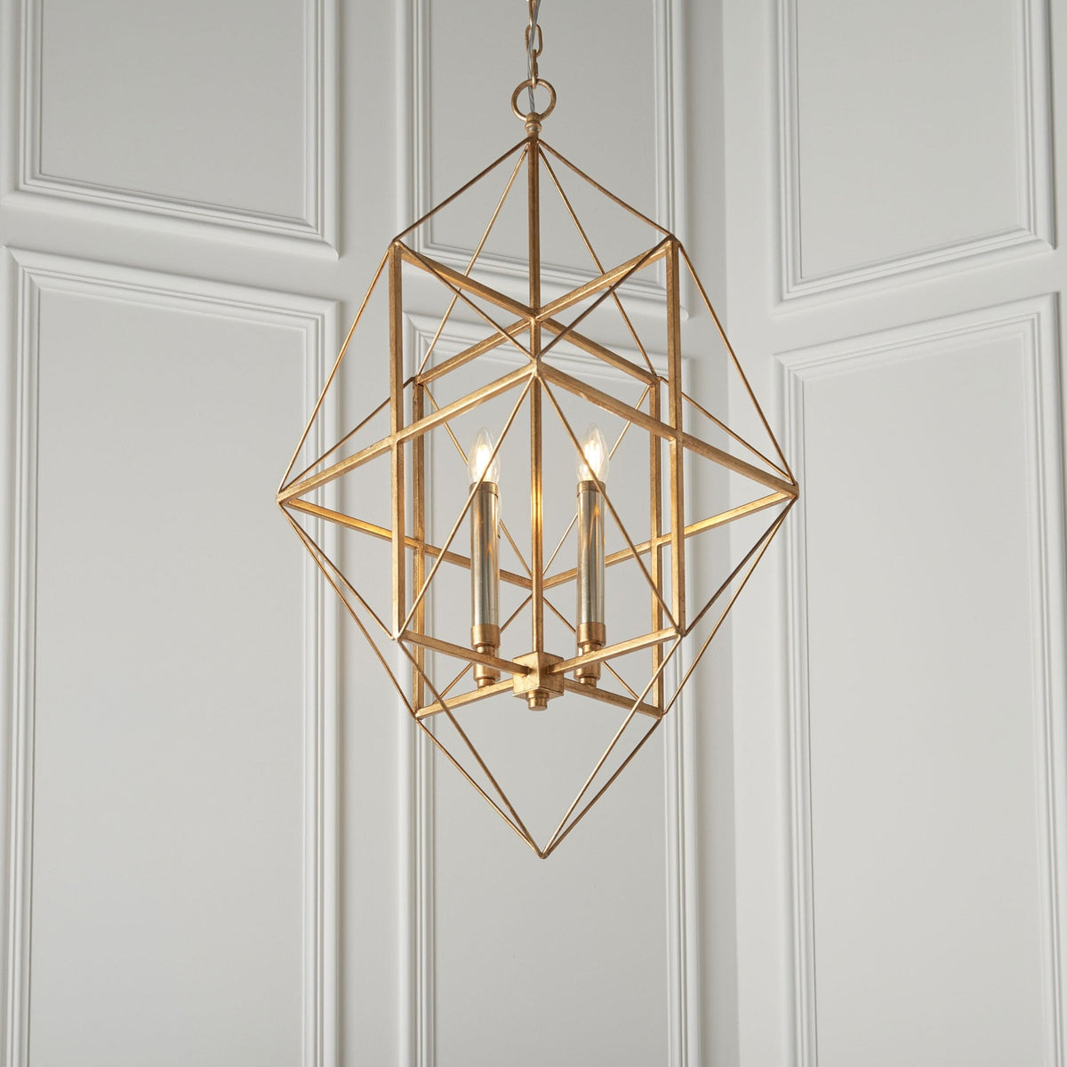 A modern gold geometric chandelier with three lights hangs in a room with white paneled walls.