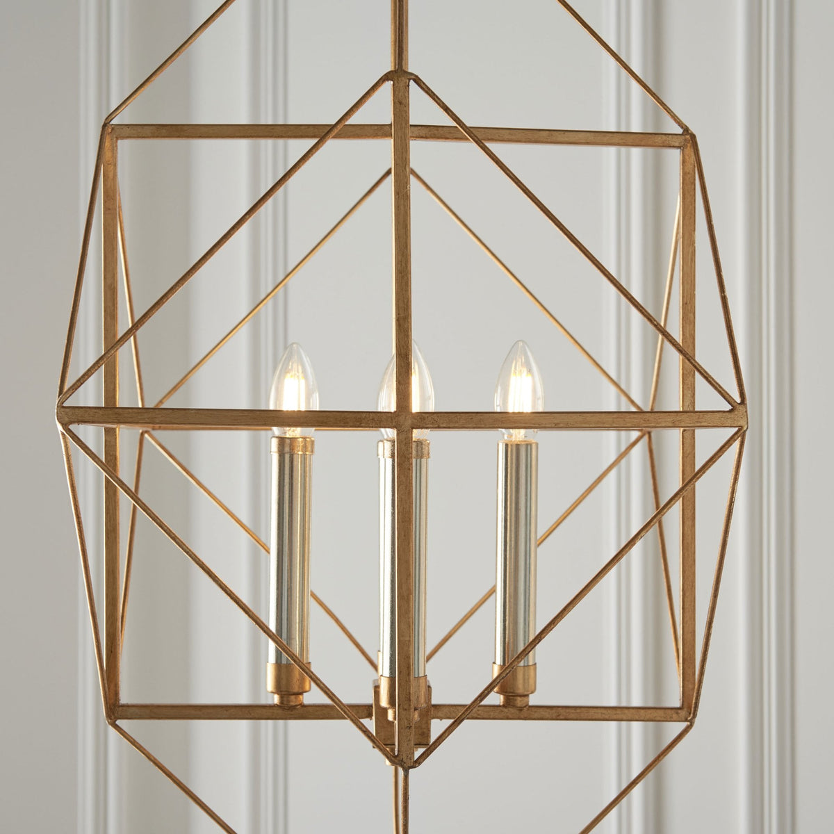 Close-up of a modern gold geometric chandelier, showing the three illuminated candle-style bulbs within.