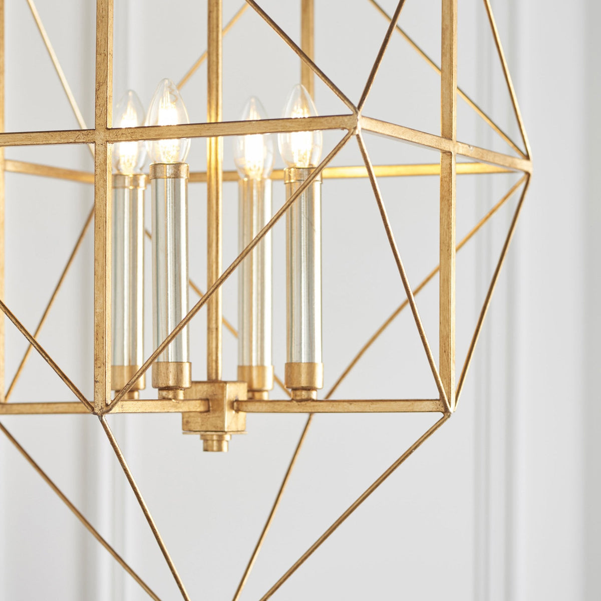 A close-up of the geometric gold chandelier highlights the four lit bulbs and intricate metalwork.