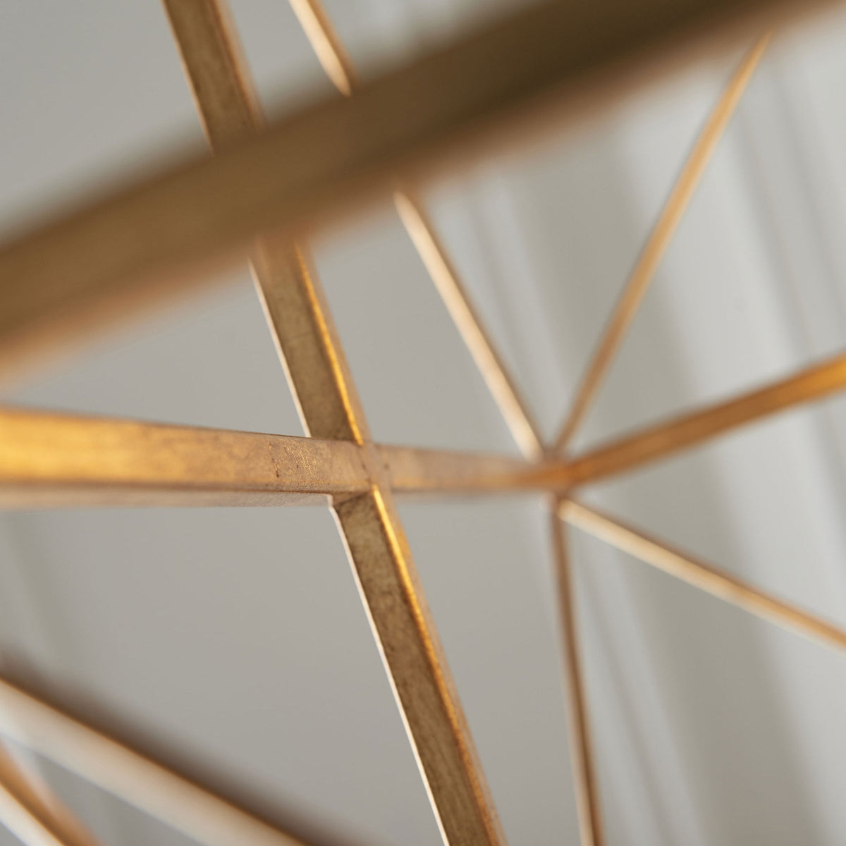 Close-up of the intersecting gold metal frame of a geometric chandelier, showcasing its intricate design.