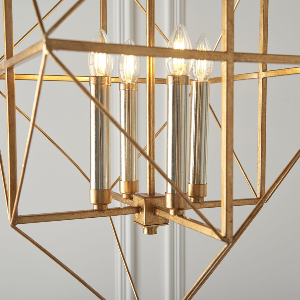A detailed view of the gold geometric chandelier shows four lit bulbs and the clear glass accents.