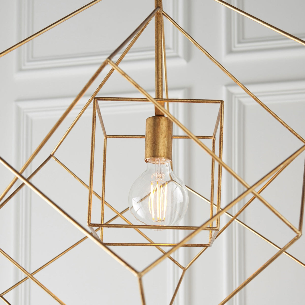 Close-up of a brass geometric pendant light with an exposed bulb, highlighting its intricate design.