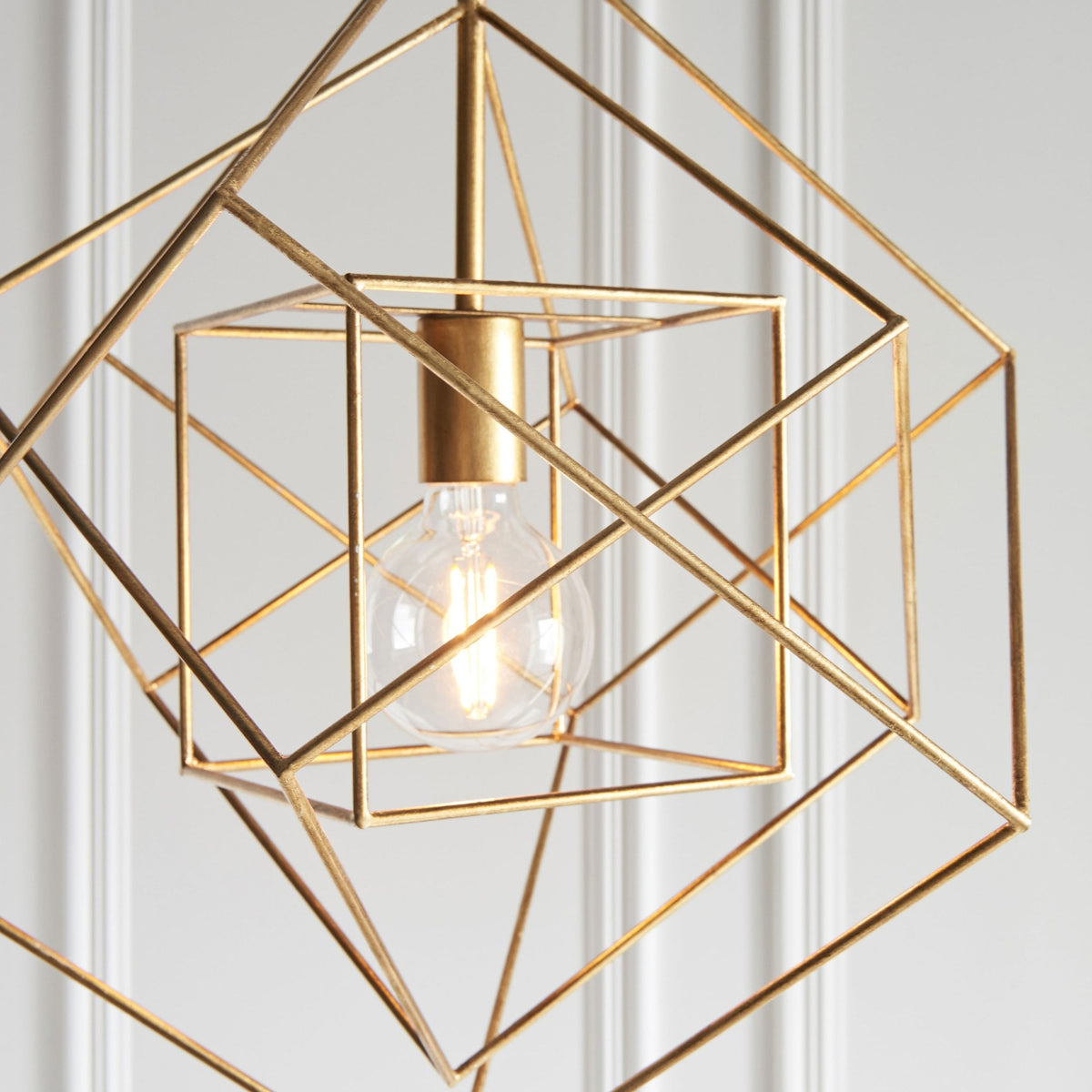 Close-up of a brass geometric pendant light with an exposed bulb, showcasing its cubic design.