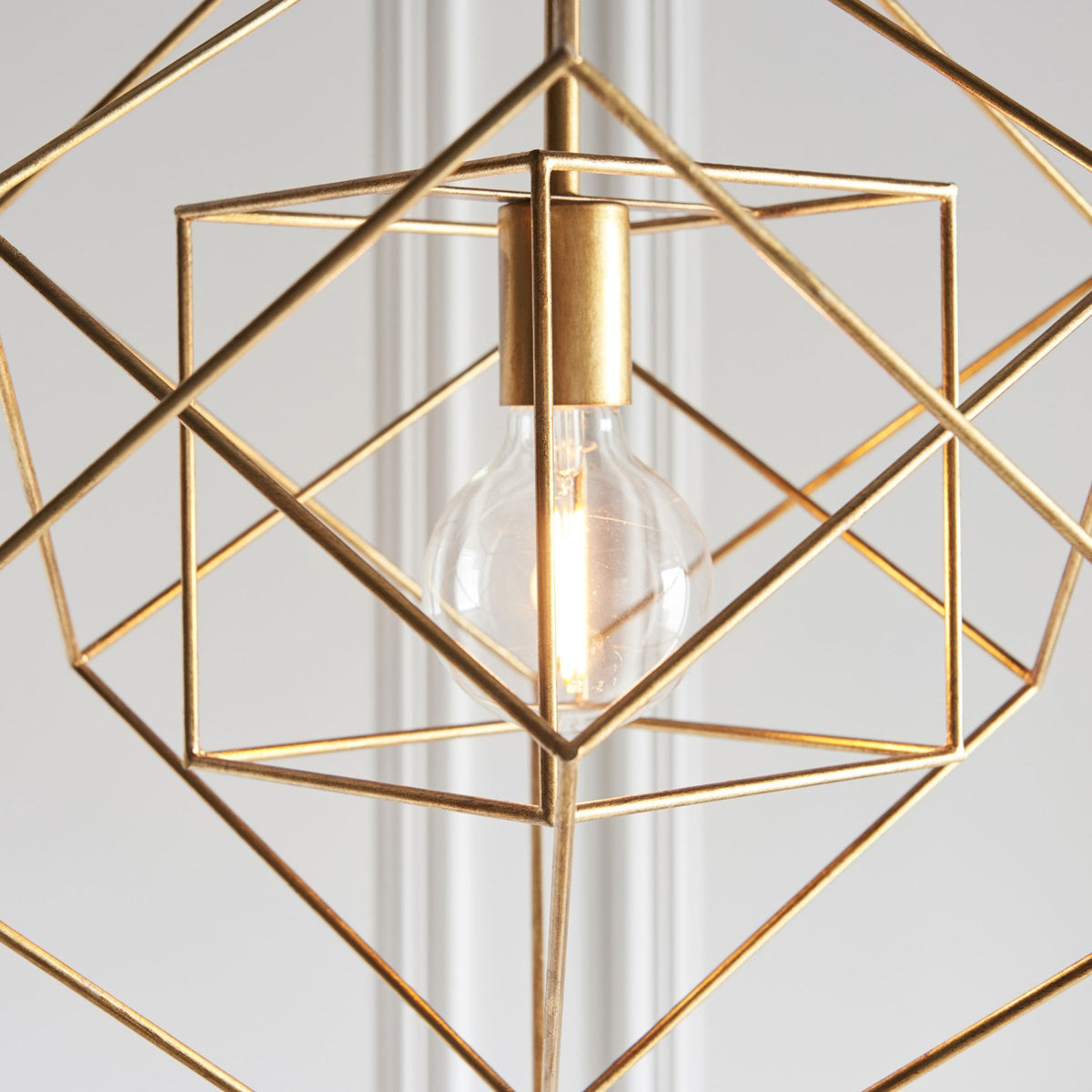 Close-up of a brass geometric pendant light, focusing on the clear bulb within the cage design.