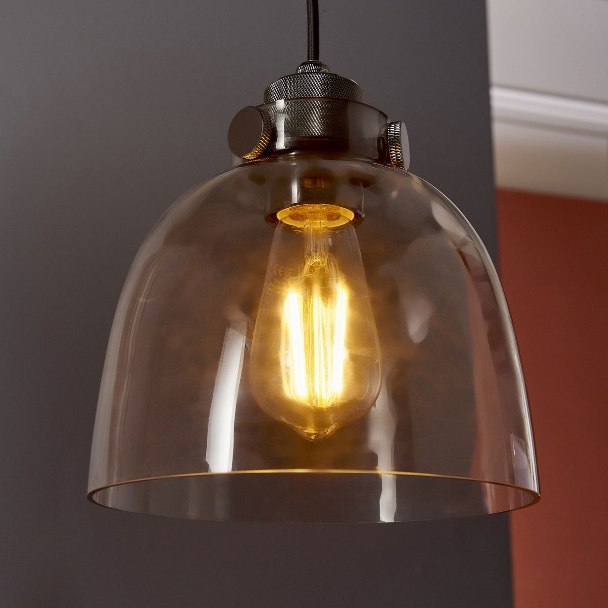 Close-up of a pendant light with a clear glass dome shade and an exposed filament bulb.