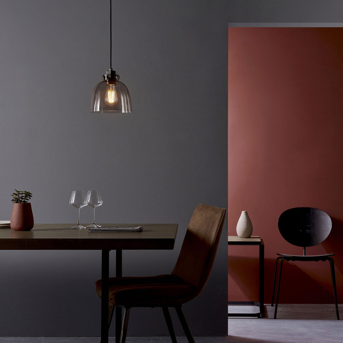 Pendant light hanging above a dining table with two chairs in a room with dark gray and red walls.