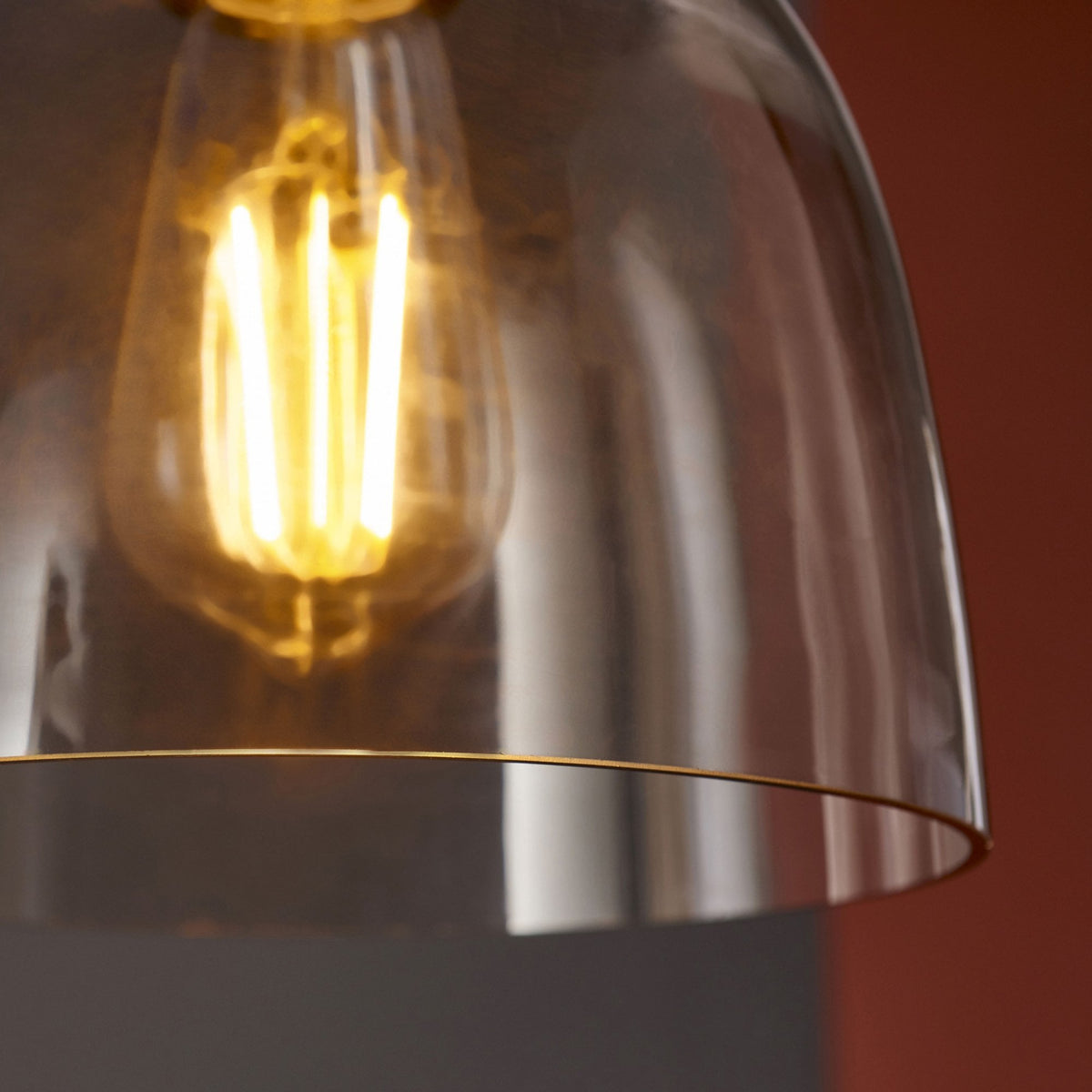 Close-up of the clear glass dome shade and glowing filament bulb of a pendant light.