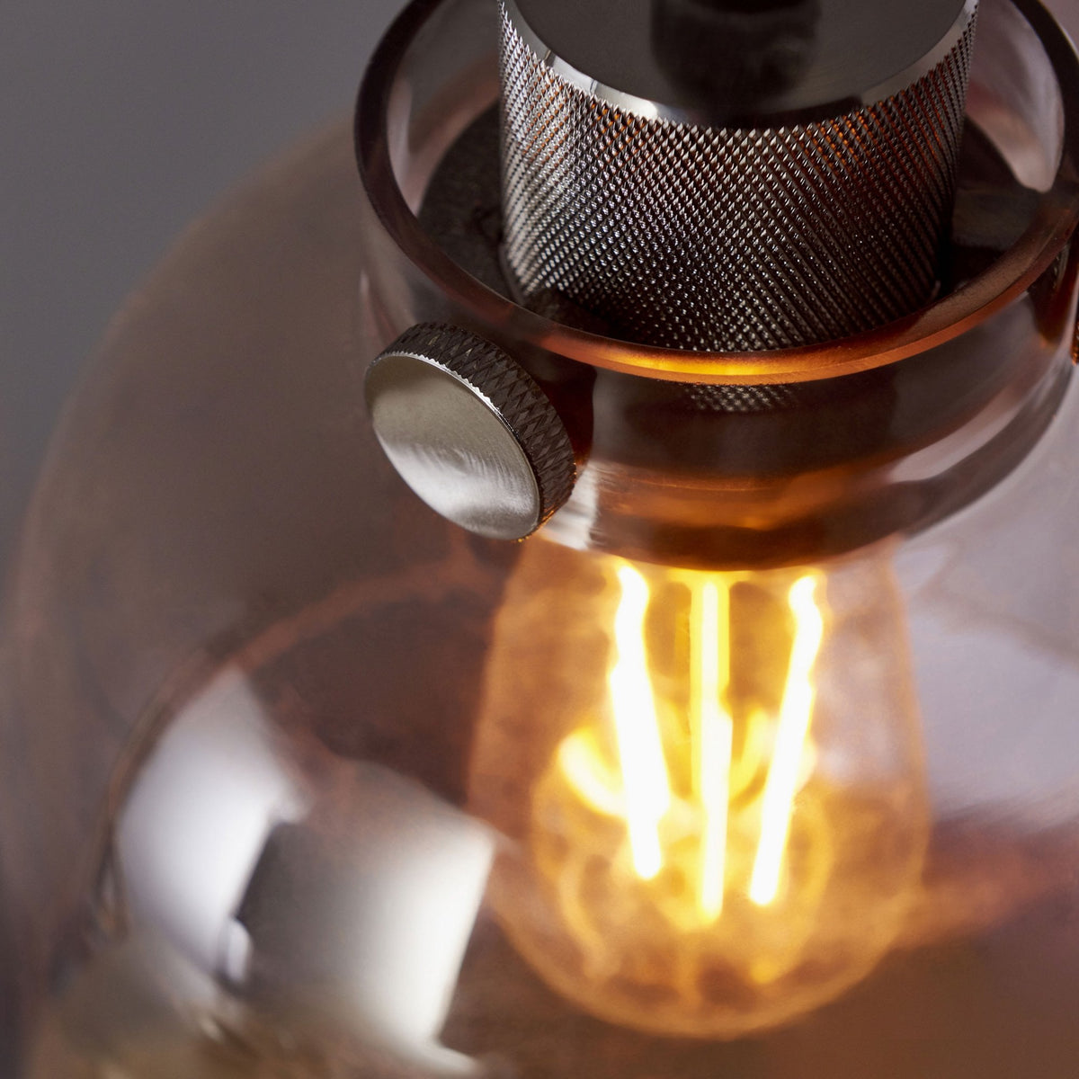 Close-up of the metal fixture and glowing filament bulb inside the clear glass shade of a pendant light.