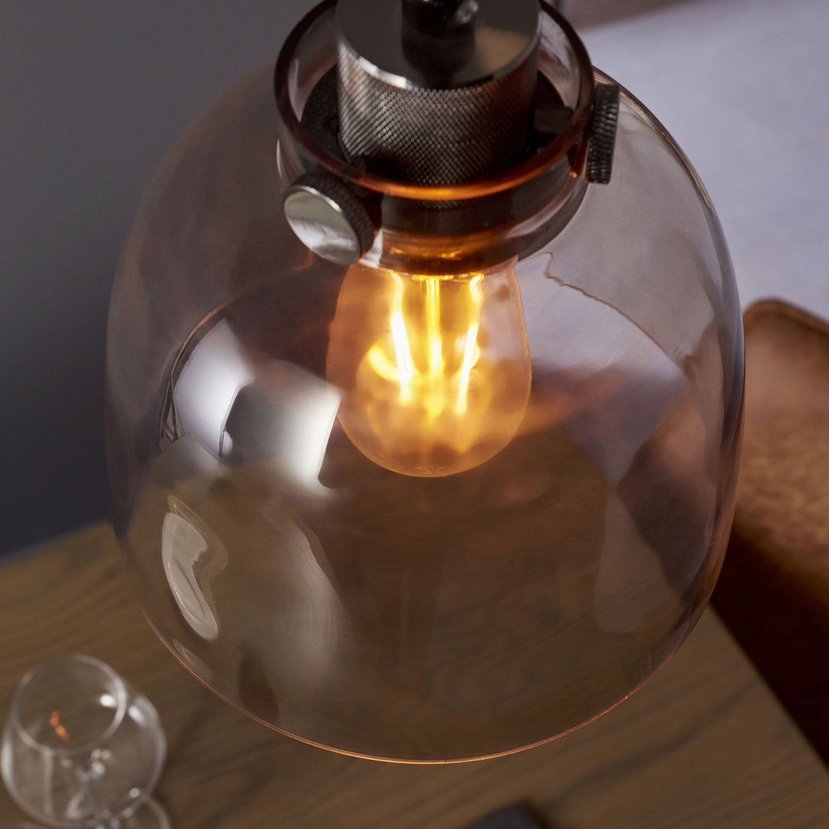 Overhead view of a pendant light with a clear glass dome shade and an exposed filament bulb, with a glass on a table below.
