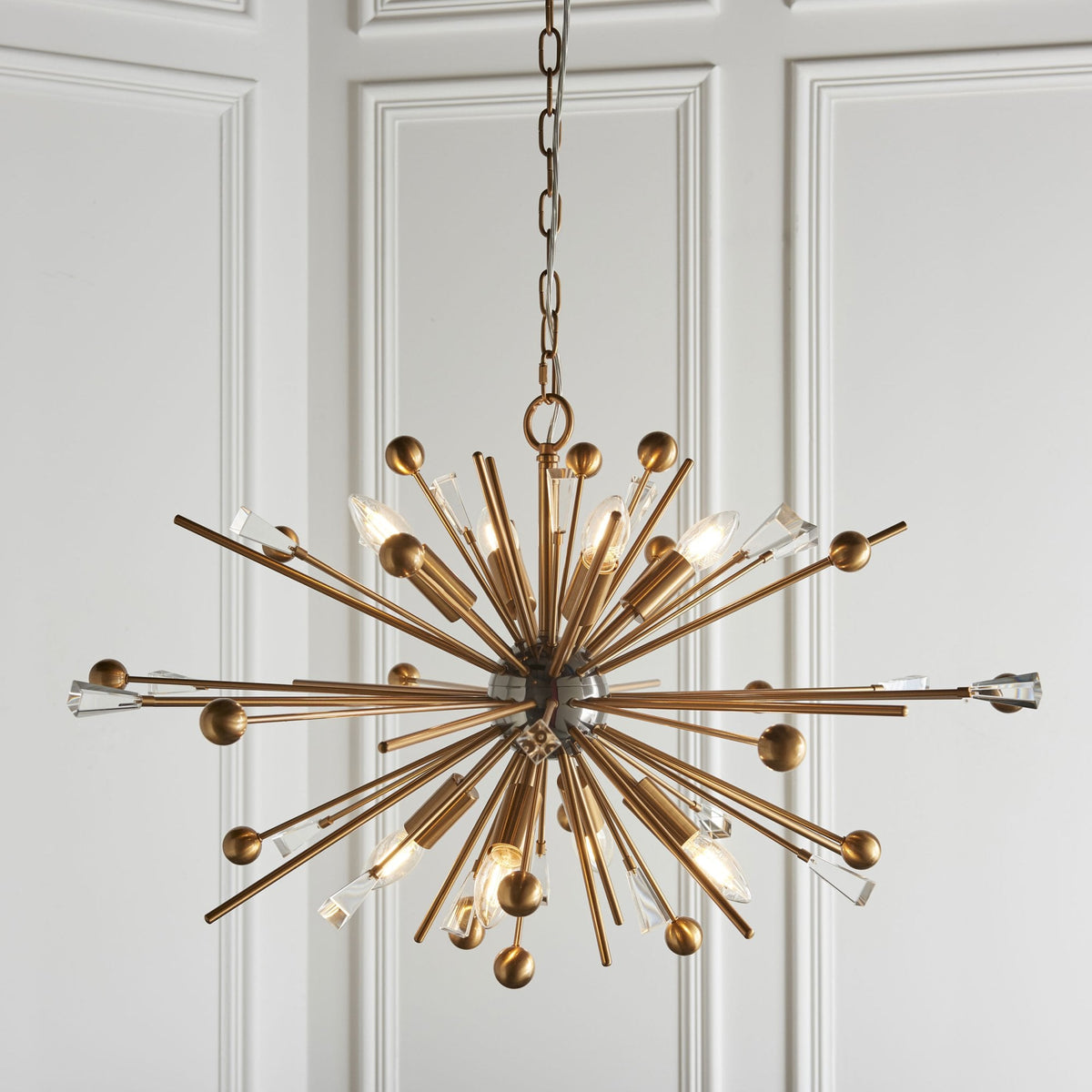 A large, sputnik-style chandelier with numerous brass rods extending outwards, some tipped with clear crystal accents.