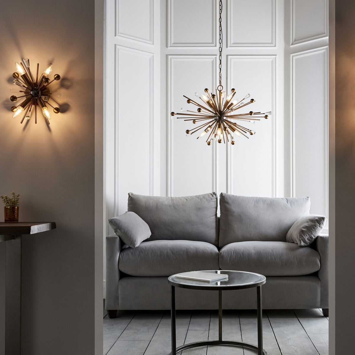 A living room with a gray sofa, a round coffee table, and a sputnik-style chandelier and matching wall sconce.