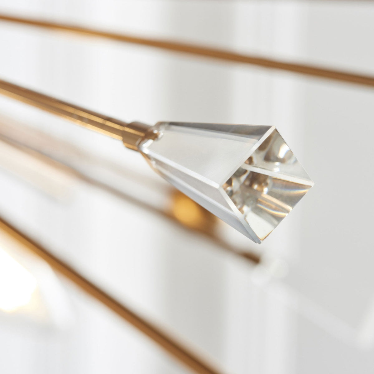 Close-up of a clear, faceted crystal accent at the end of a brass rod on a chandelier.
