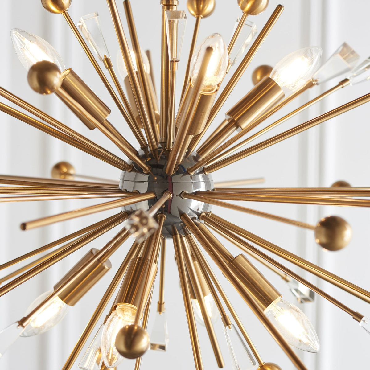 A close-up, worm's-eye view of a sputnik-style chandelier with brass rods, light bulbs, and crystal accents.