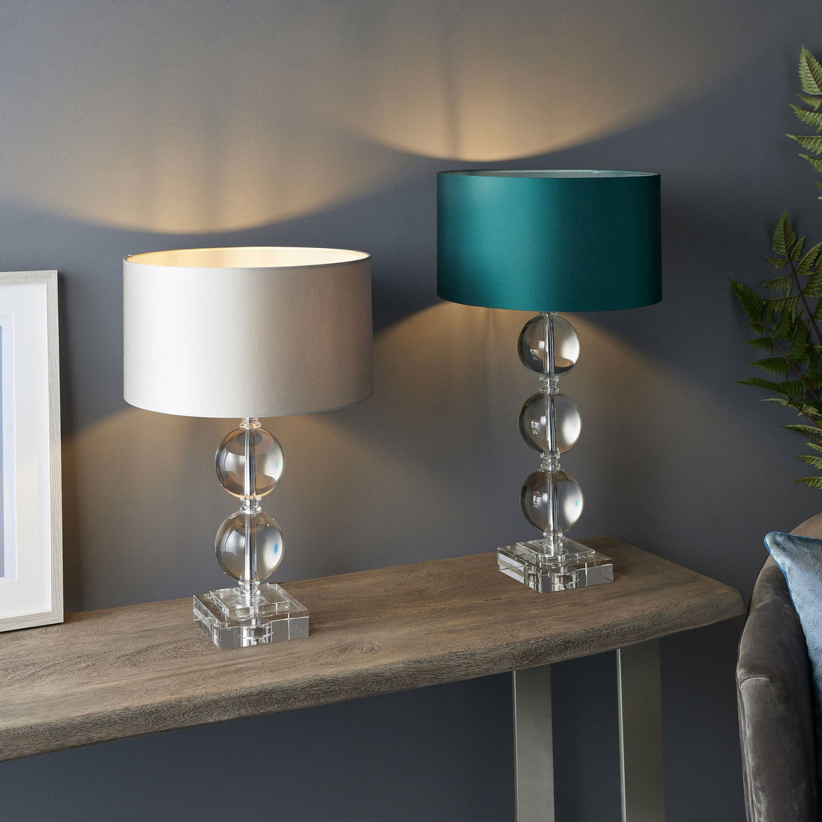 Two table lamps on a wooden console table, one with a light grey shade and one with a teal shade.