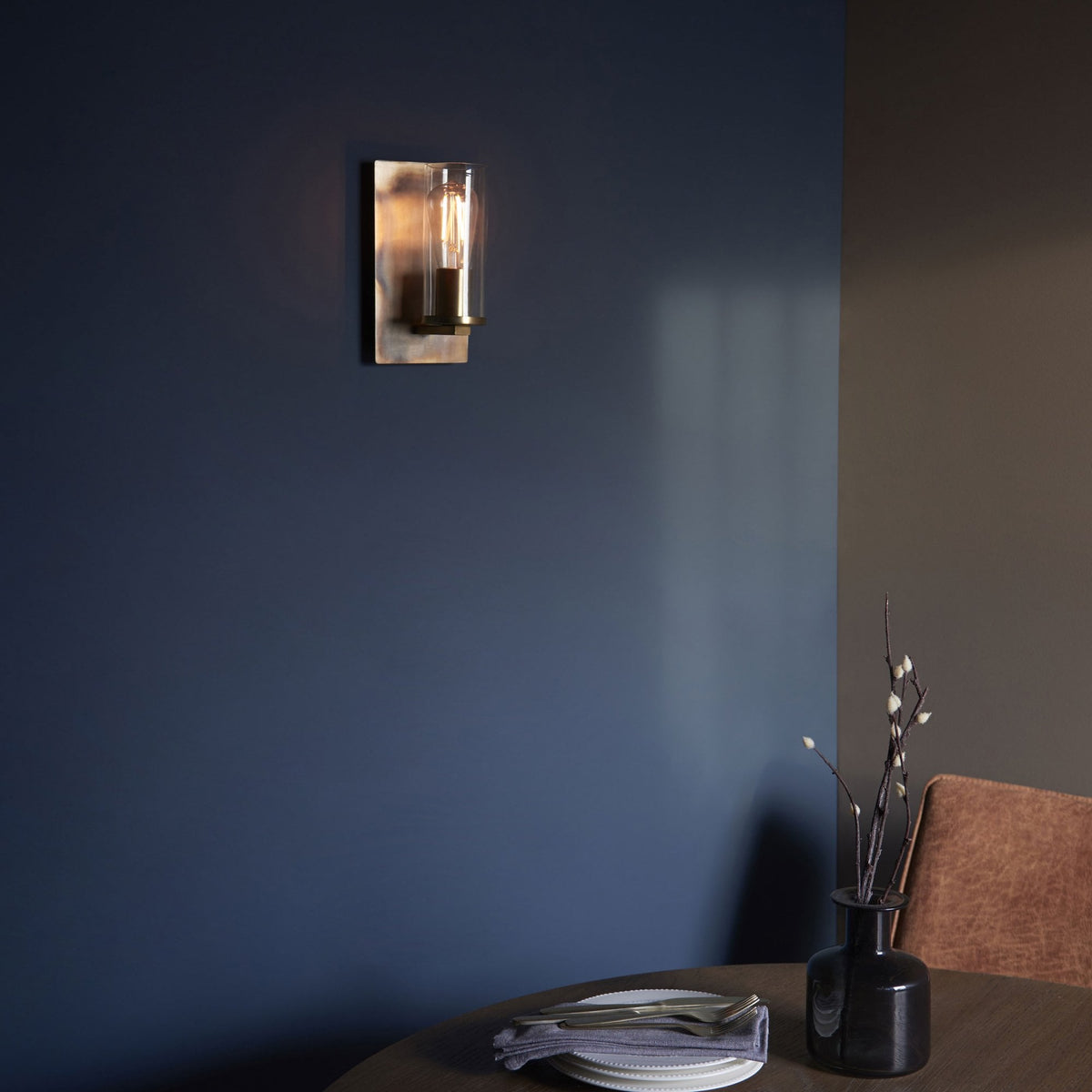 A wall light mounted on a dark blue wall, casting a warm glow over a wooden table.