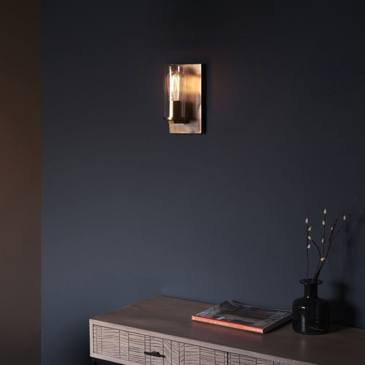 A wall light on a dark blue wall above a wooden console table, creating an inviting ambiance.