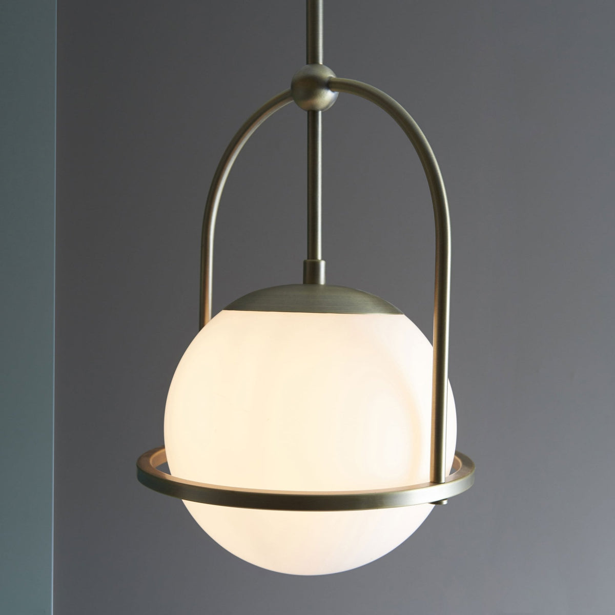 A close-up of a modern bronze pendant light with a spherical white glass shade illuminating a room.