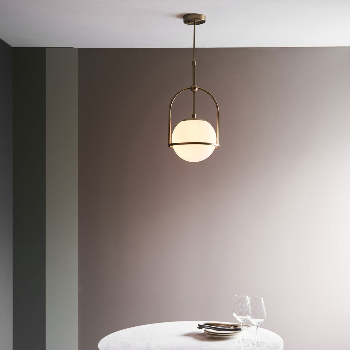 A modern bronze pendant light with a spherical white glass shade hangs above a round white table.