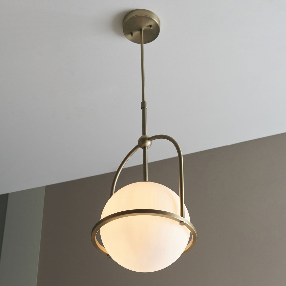 A bronze pendant light with a spherical white glass shade casting a warm glow in a room.