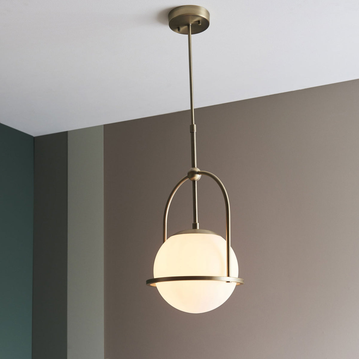 A bronze pendant light with a spherical white glass shade hanging in a room with a two-tone wall.
