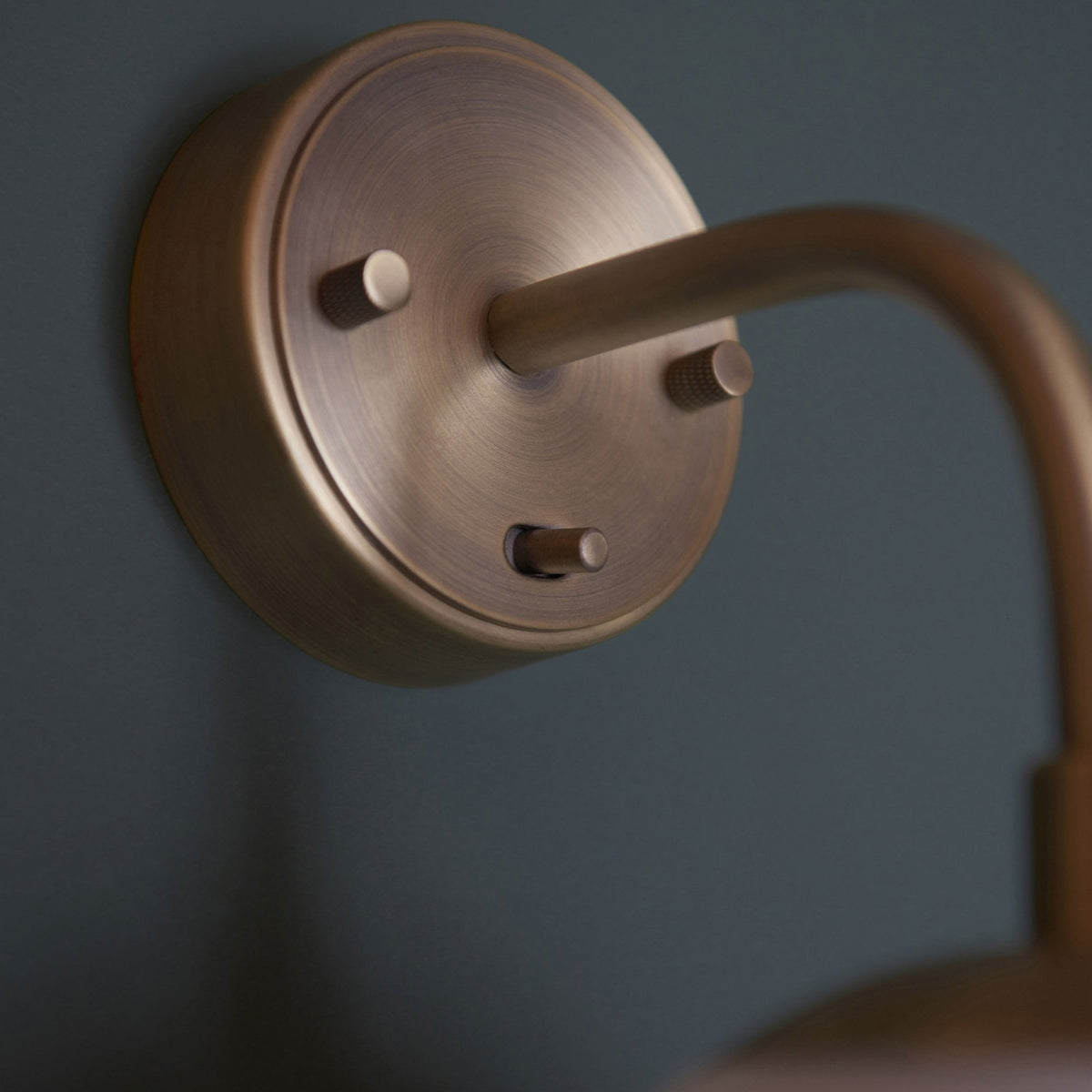 A close-up of the brass wall mount of a light fixture on a dark green wall.