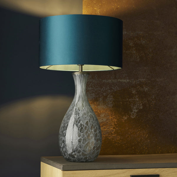 Grey crackle glass table lamp with a teal shade on a wooden surface.