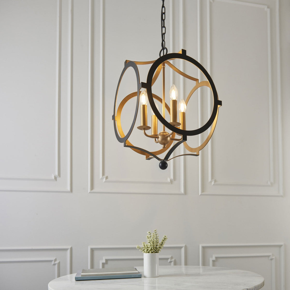 A black and gold chandelier hangs above a white marble table in a room with white paneled walls.