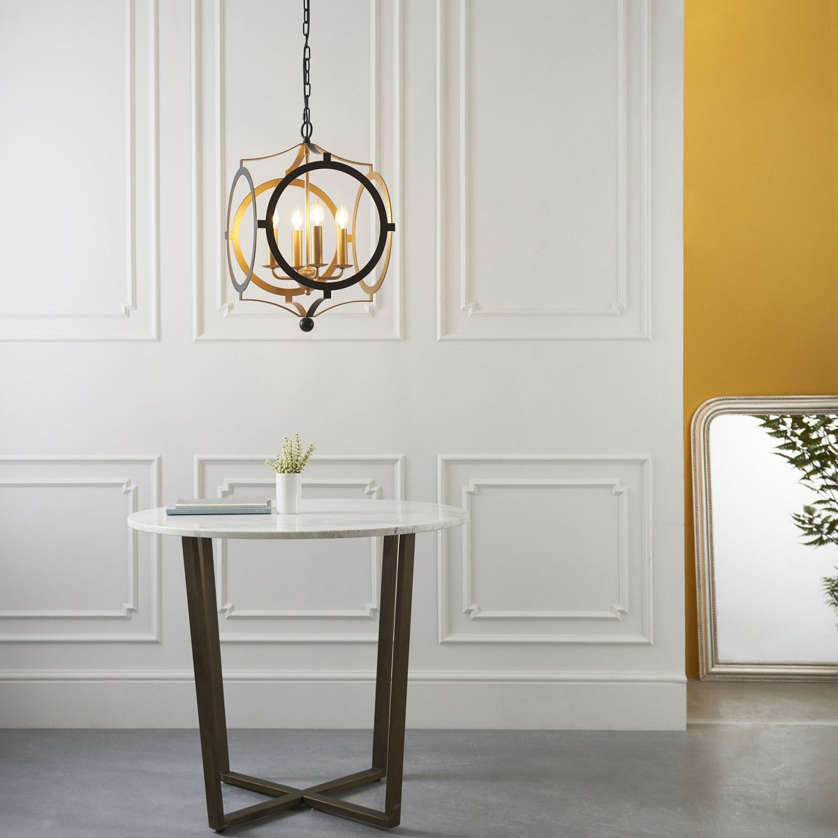 A black and gold chandelier hangs in a room with a round table and a large mirror.