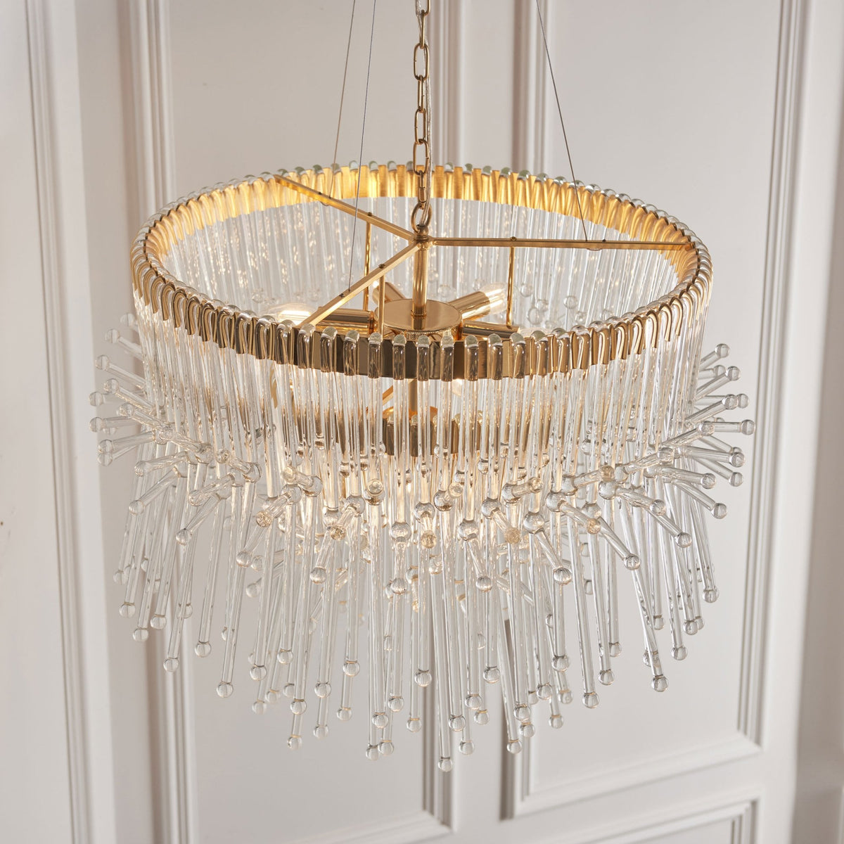 Top-down view of a two-tier gold and clear glass chandelier with a white paneled wall.